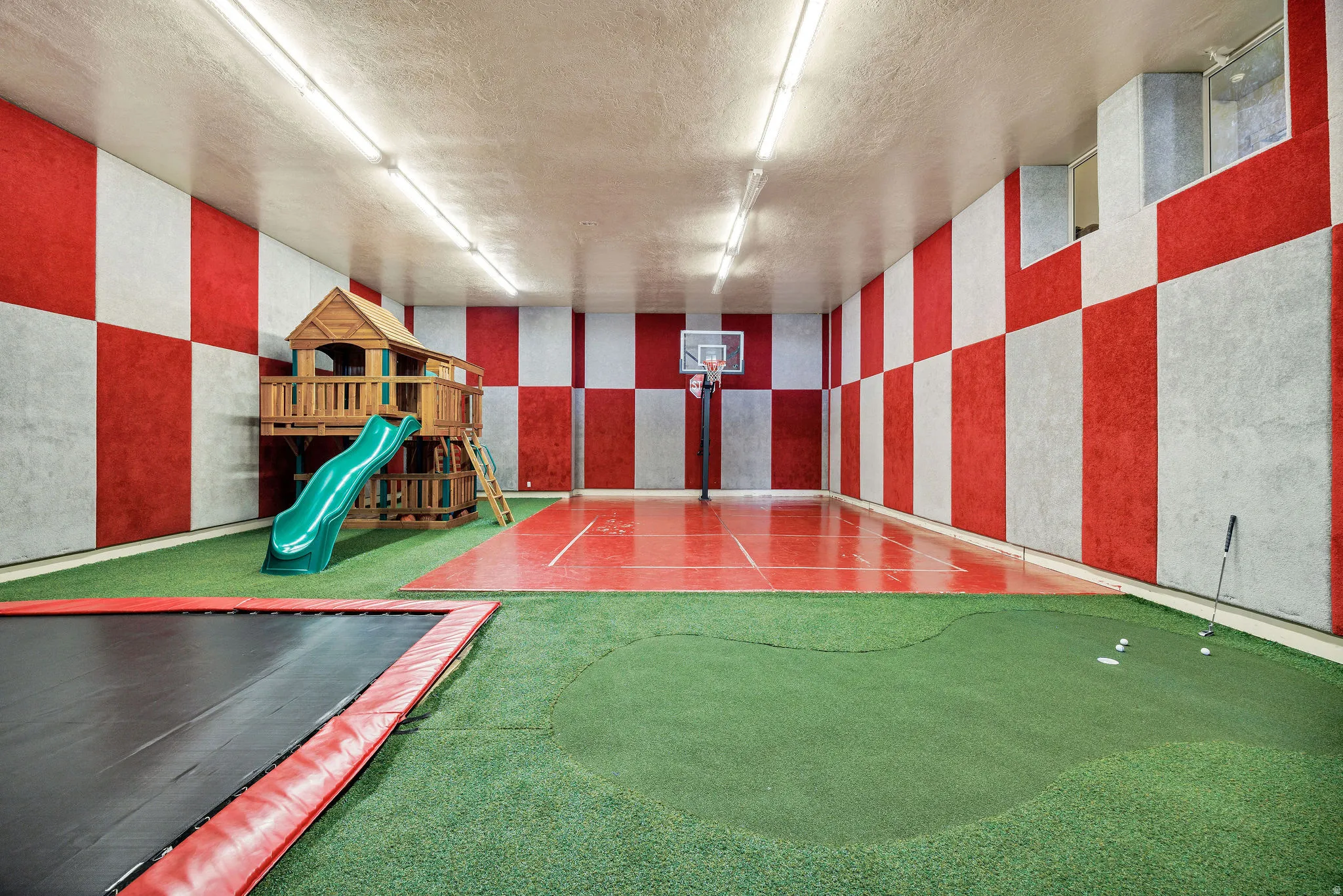 Dedicated indoor recreation space featuring a basketball court, putting green, and built-in trampoline