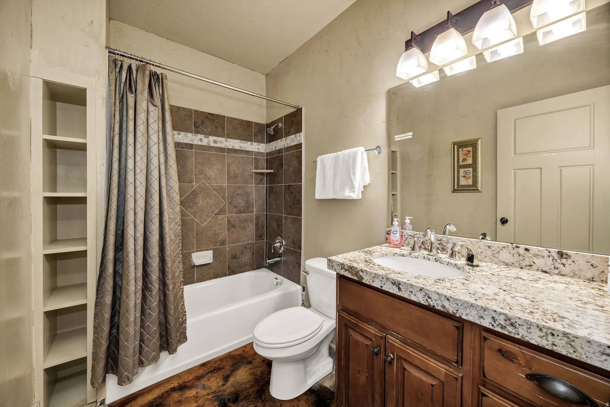 Bathroom featuring a white tub, brown tiled shower surround with accent band, built-in shelving, and a vanity with a white-toned countertop