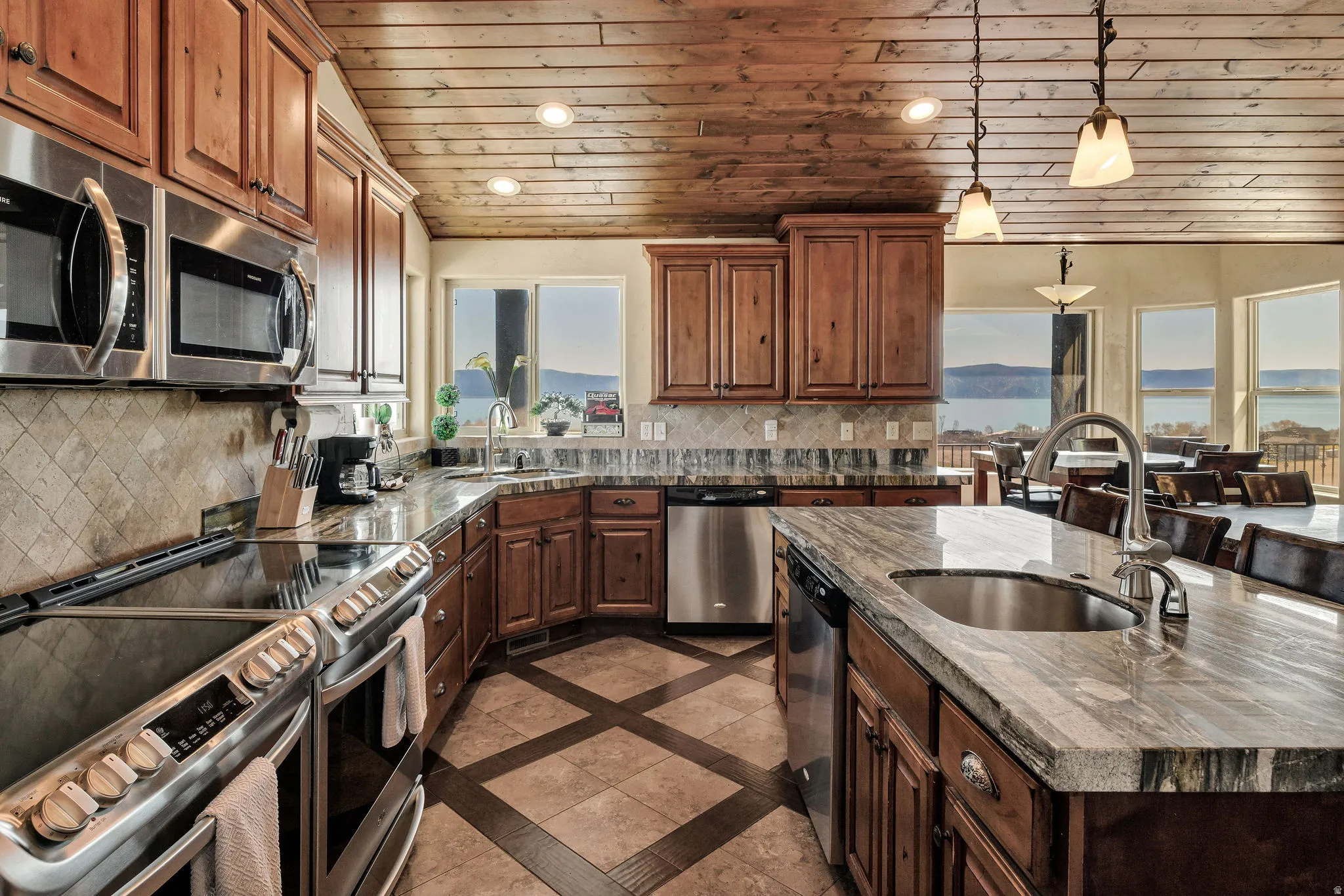 Spacious kitchen featuring warm wood cabinetry, stainless steel appliances, patterned tile backsplash, multi-toned countertops, and a wood-planked vaulted ceiling