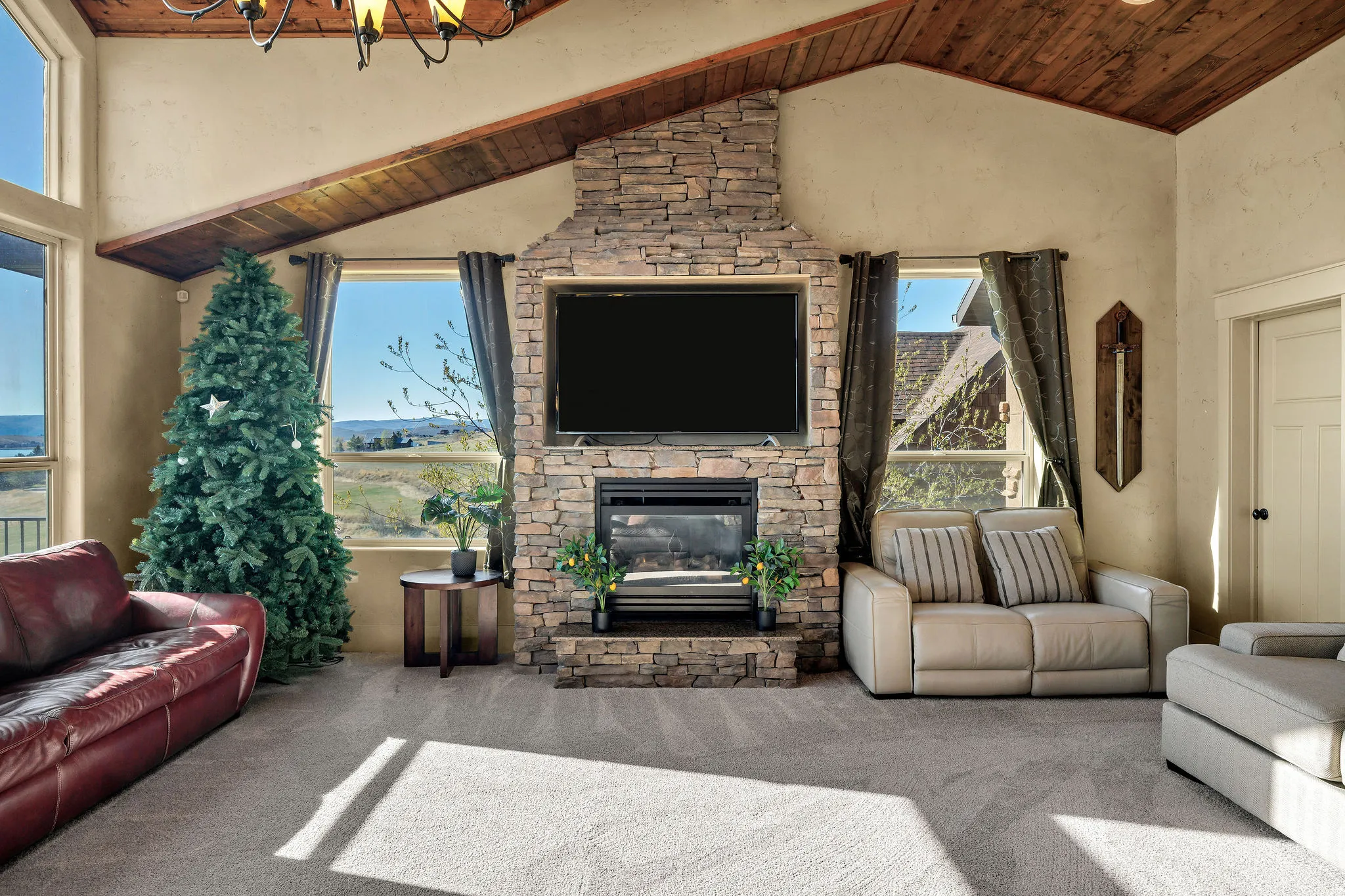 Living area featuring a stone-clad fireplace with built-in media space, vaulted wood-plank ceiling, expansive windows, and light-toned carpet flooring