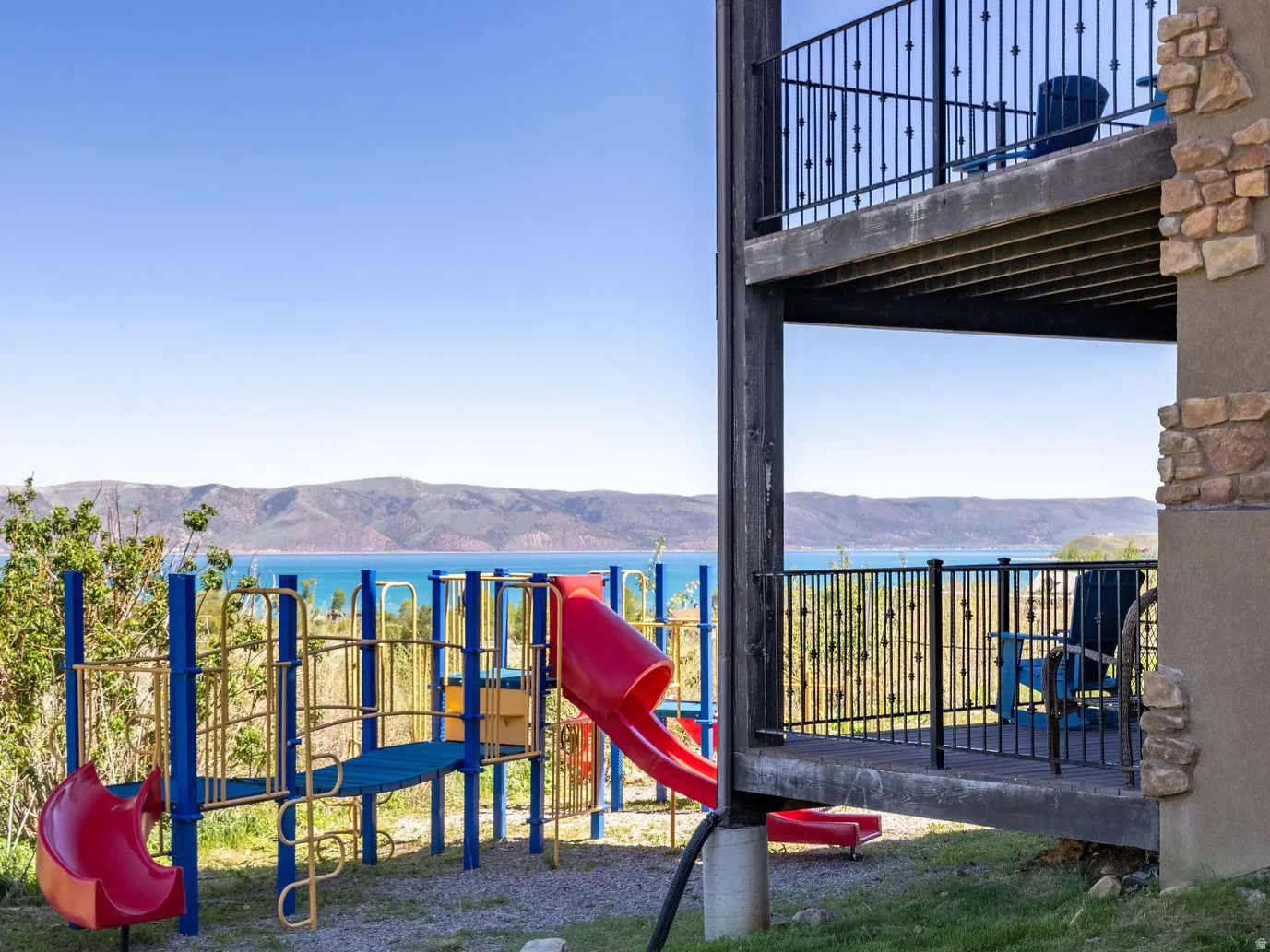 Terraced exterior featuring two levels of balconies with black metal railings, a stone accent facade, and a ground-level play structure