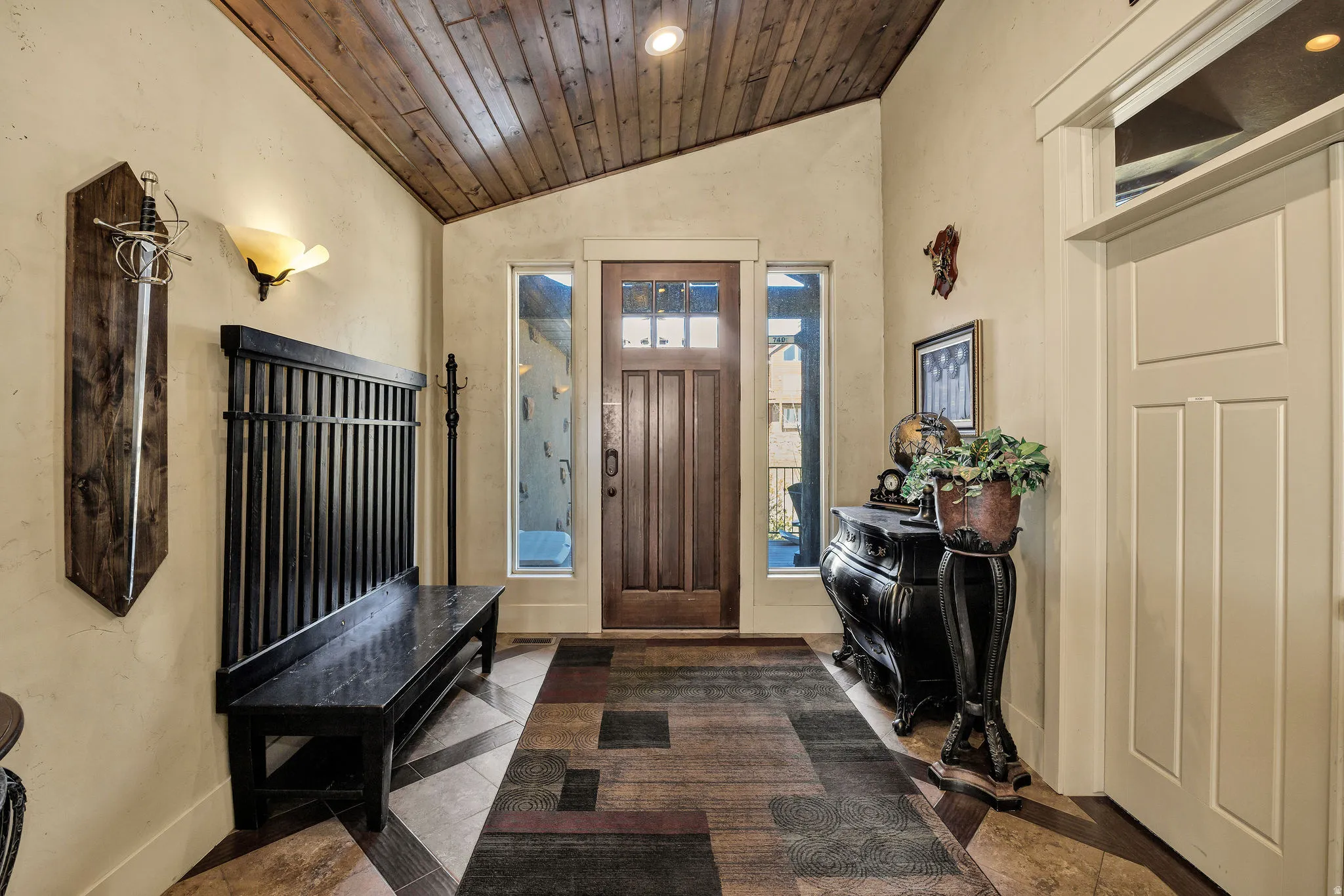 Foyer featuring a wood-panel accent ceiling, solid wood entry door with clear glass panels, side light windows, and tile flooring with a geometric pattern