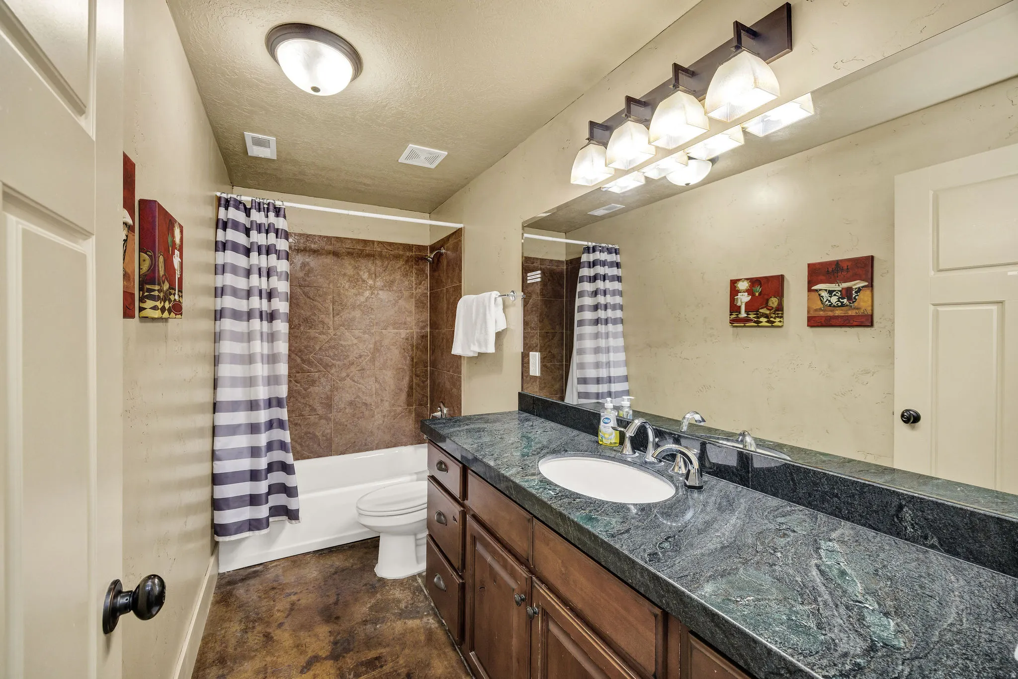 Bathroom featuring a dark wood vanity with an integrated sink, a dark patterned countertop, and a wide mirror with a five-light fixture