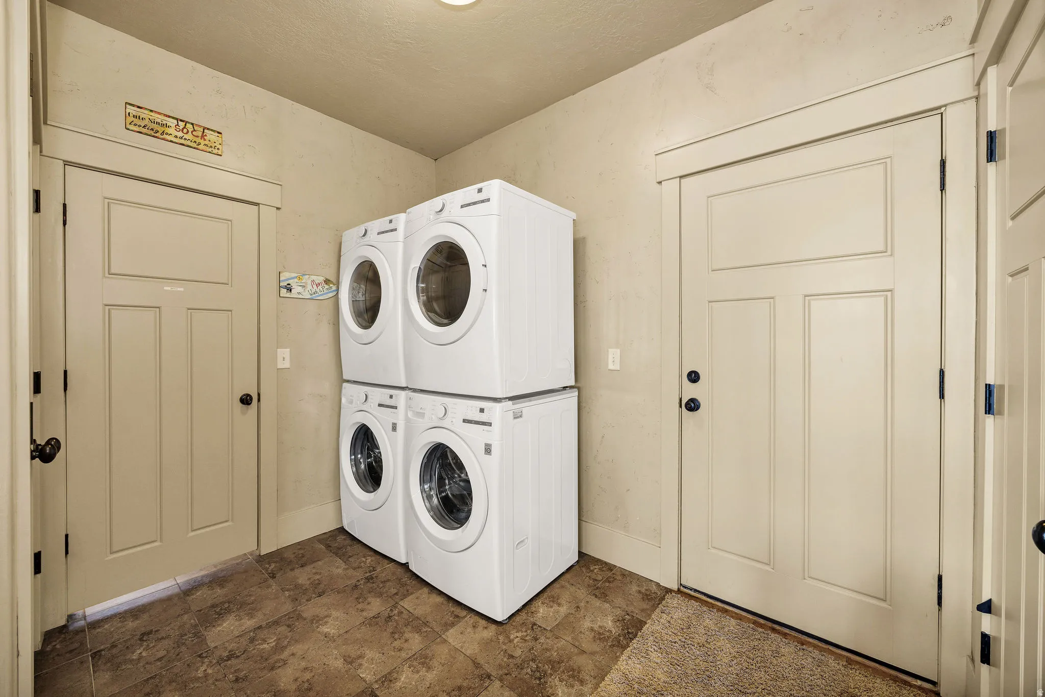 Dedicated laundry area featuring dual stackable washer and dryer units, neutral wall paint, and durable tile flooring