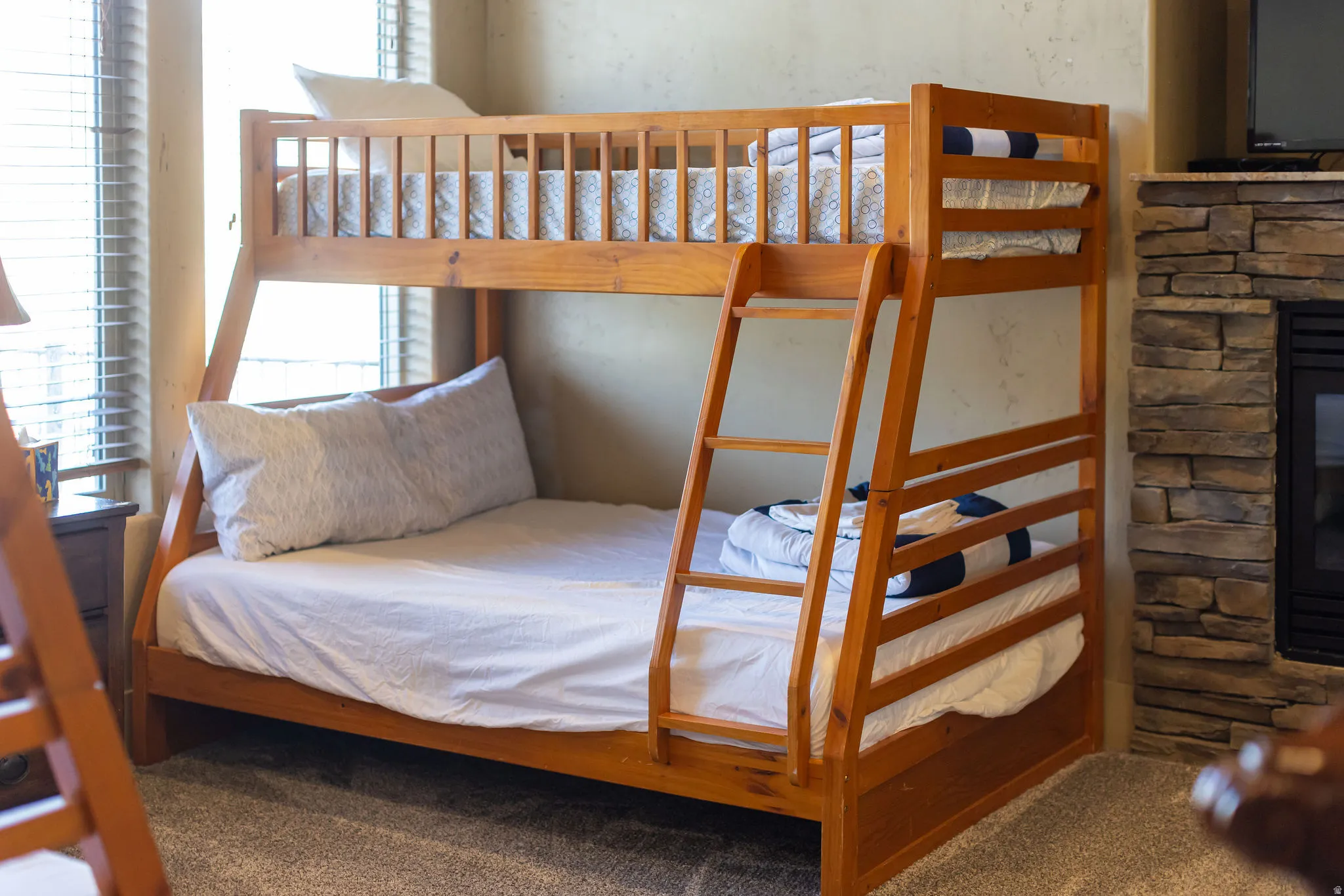 Wood-finish bunk bed with integrated ladder, accompanied by a stone-clad fireplace and hearth