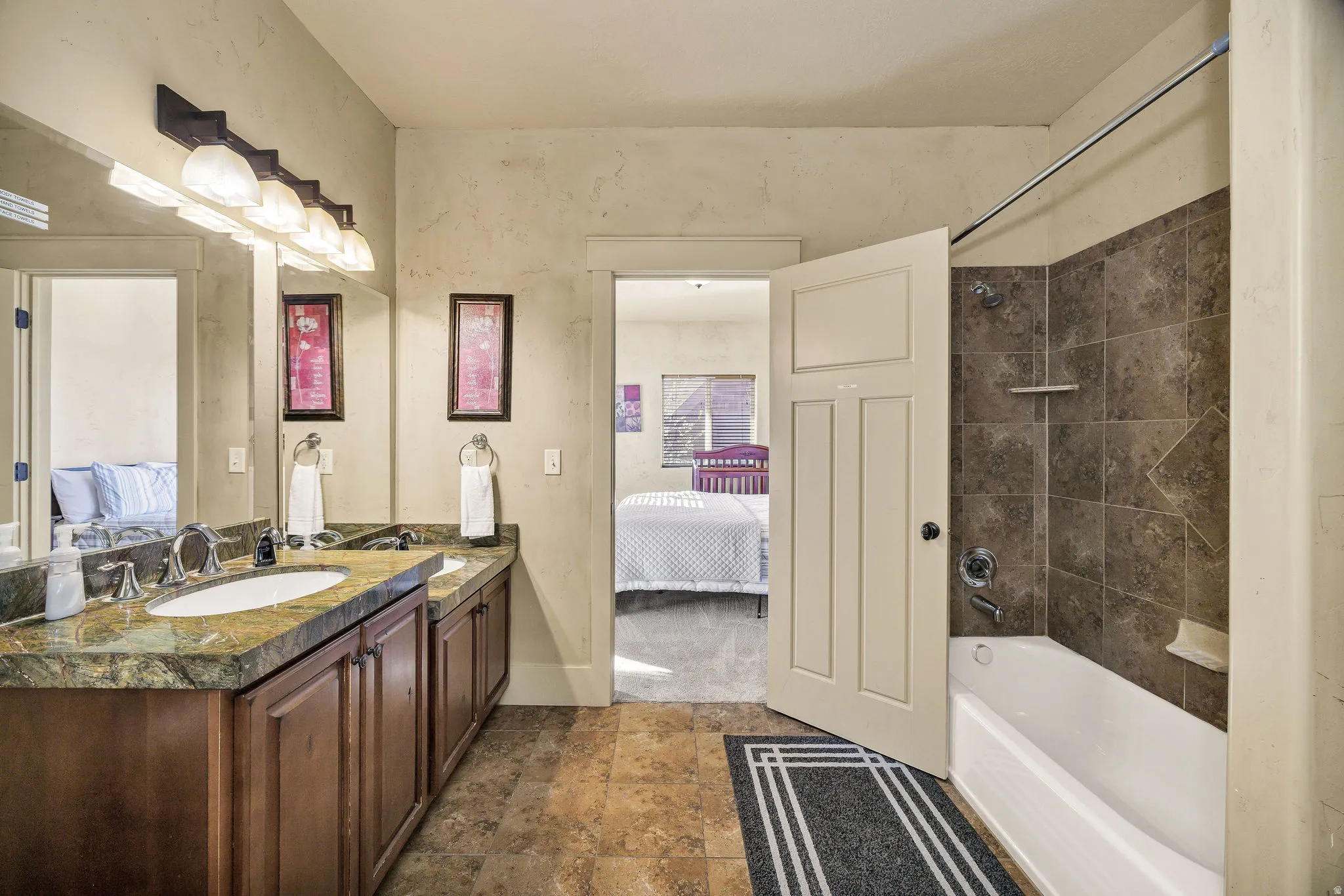 Bathroom featuring a dual vanity with a patterned countertop, integrated sinks, and wood cabinetry