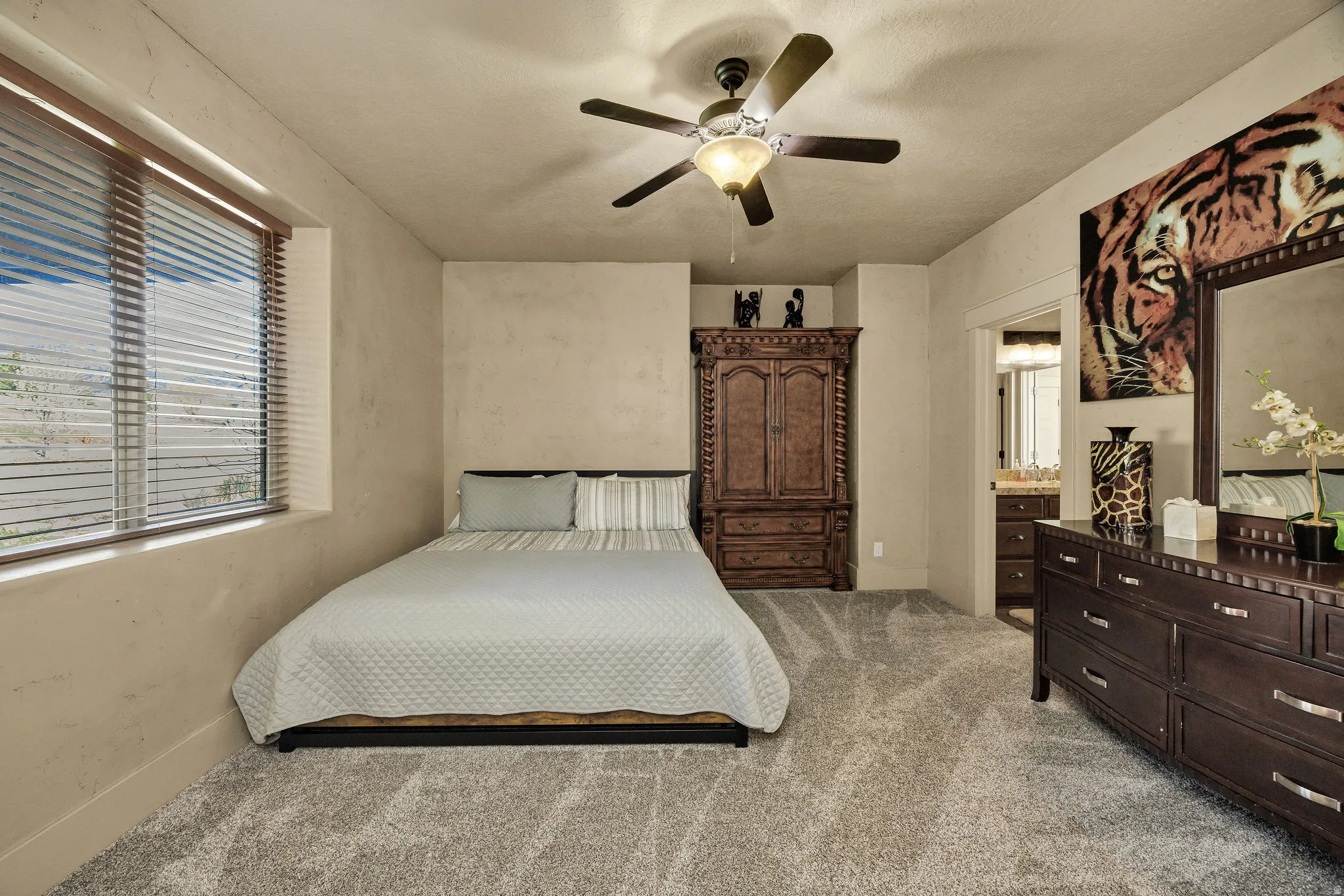 Spacious room featuring plush gray carpet, a ceiling fan with integrated lighting, and a large window with blinds