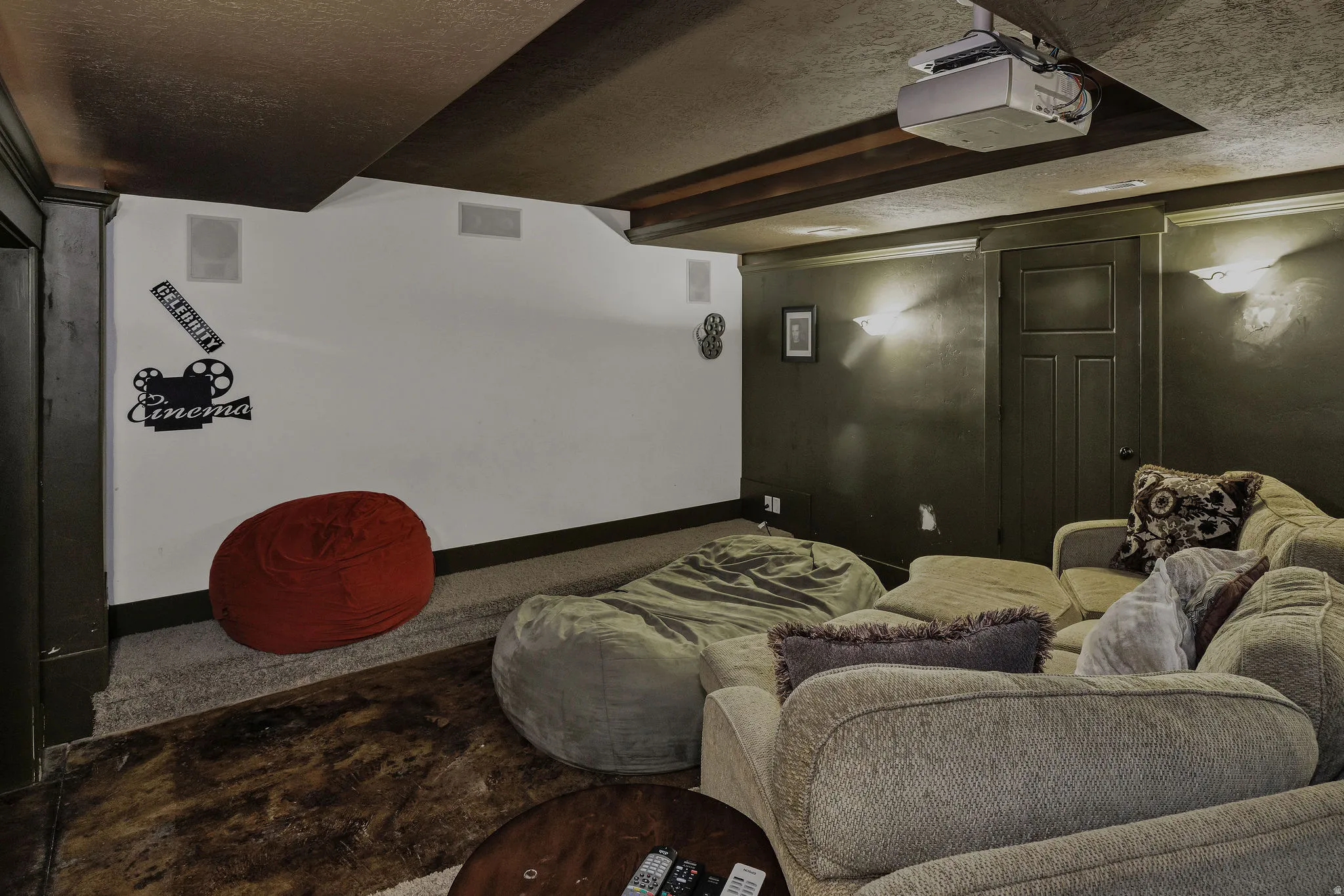 Dedicated media room with a ceiling-mounted projector, built-in ceiling speakers, recessed wall lighting, and a dark accent wall