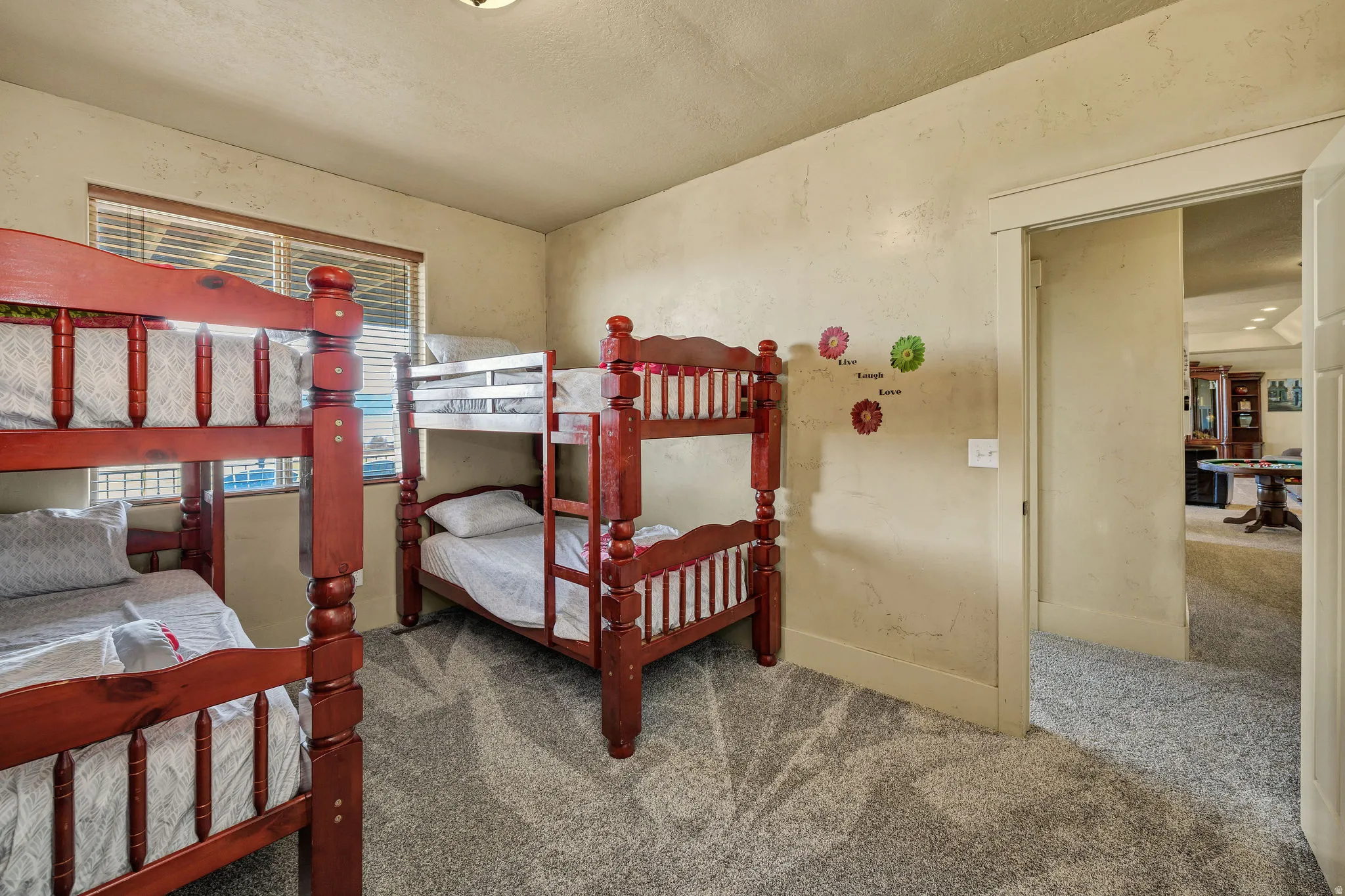 Carpeted room featuring textured walls, a single window with blinds, and a doorway opening to another interior space