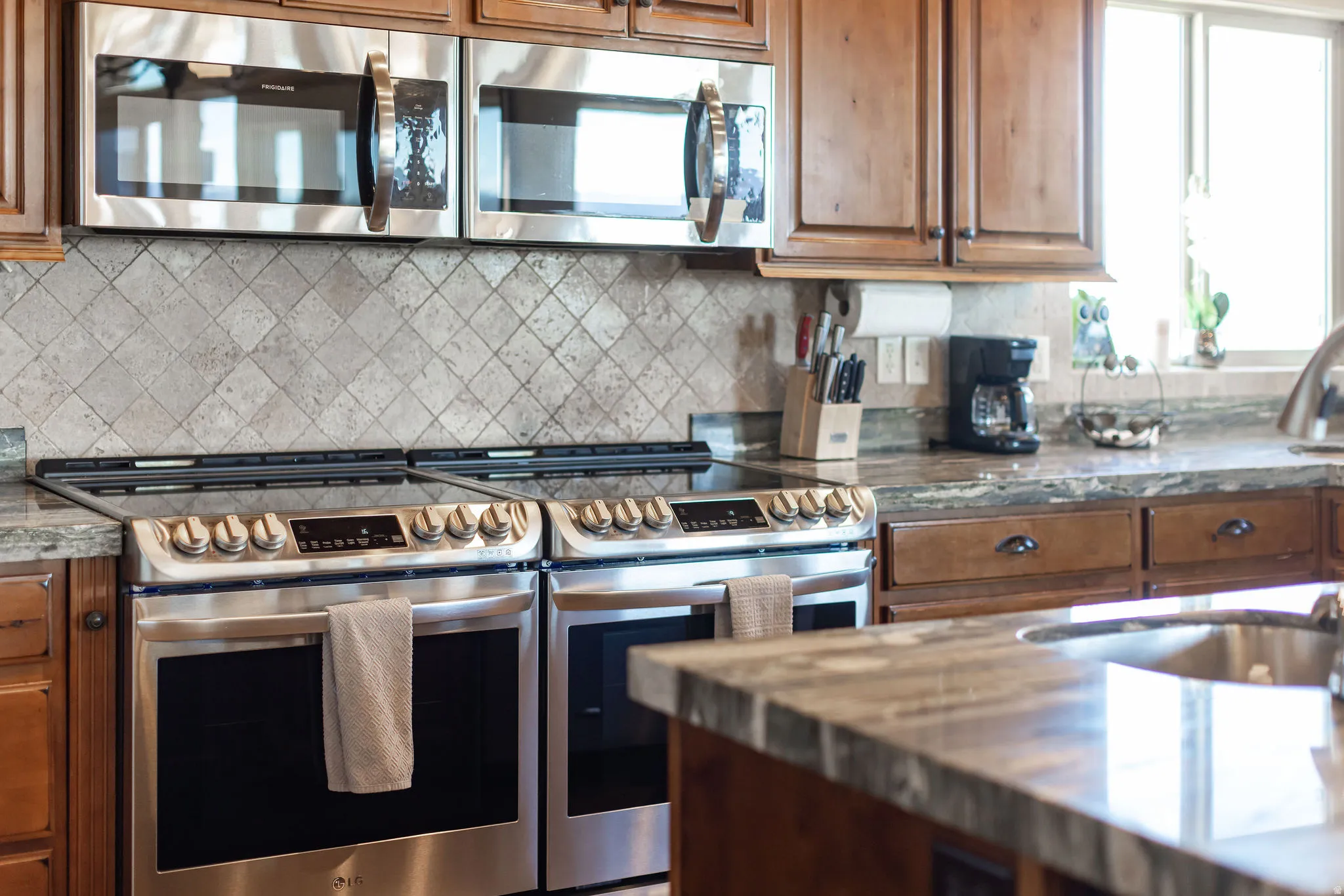 Kitchen showcasing dual stainless steel electric ranges, matching built-in microwaves, and a patterned tile backsplash