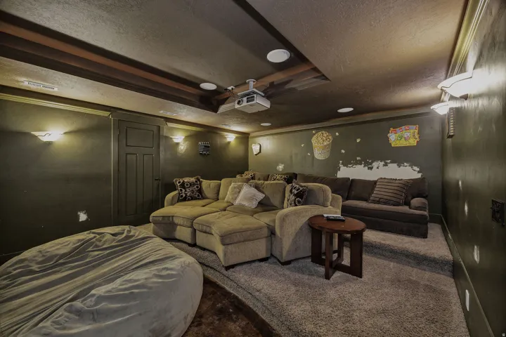 Dedicated media room featuring tiered seating, recessed ceiling lighting, wall sconces, and a ceiling-mounted projector
