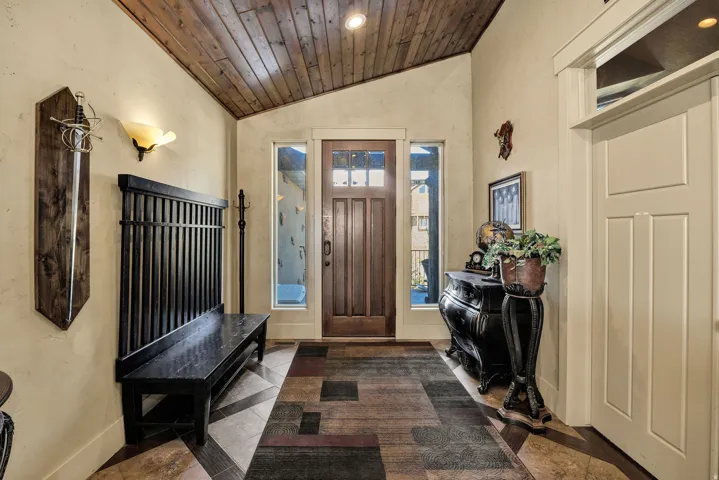 Foyer featuring a wood-panel accent ceiling, solid wood entry door with clear glass panels, side light windows, and tile flooring with a geometric pattern