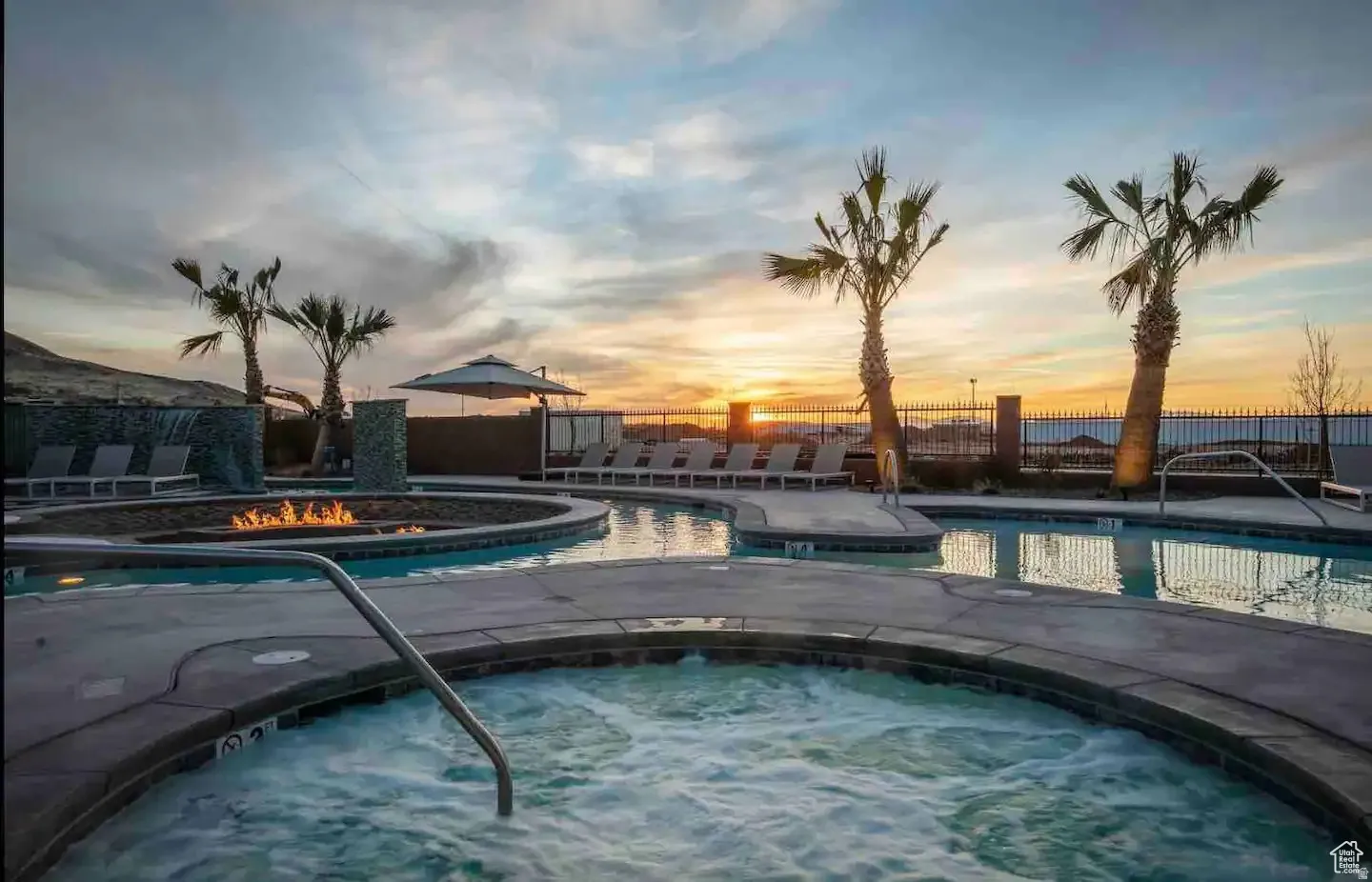 Expansive pool area featuring a large spa with a stainless steel handrail, a fire pit, and multiple lounge chairs