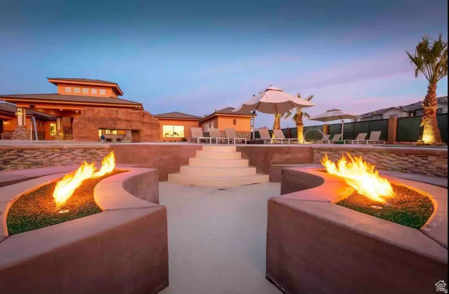 Expansive outdoor space featuring dual built-in fire pits, terraced concrete steps, a multi-level patio, stacked stone accents, and stucco exterior finishes