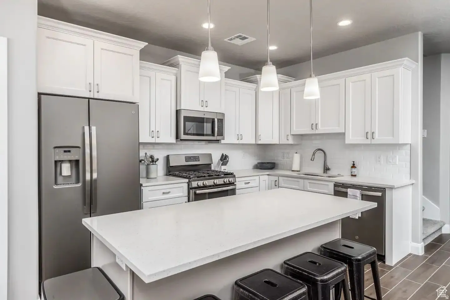 Modern kitchen featuring a central island with countertop seating, white shaker cabinetry, stainless steel appliances, and a subway tile backsplash