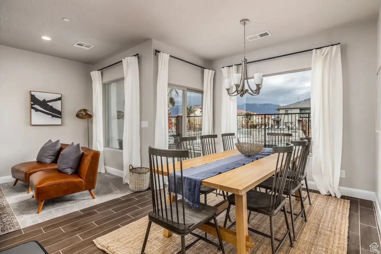 Spacious dining area featuring wood-finish flooring, a contemporary chandelier, large windows with a mountain backdrop, and light-toned wall paint
