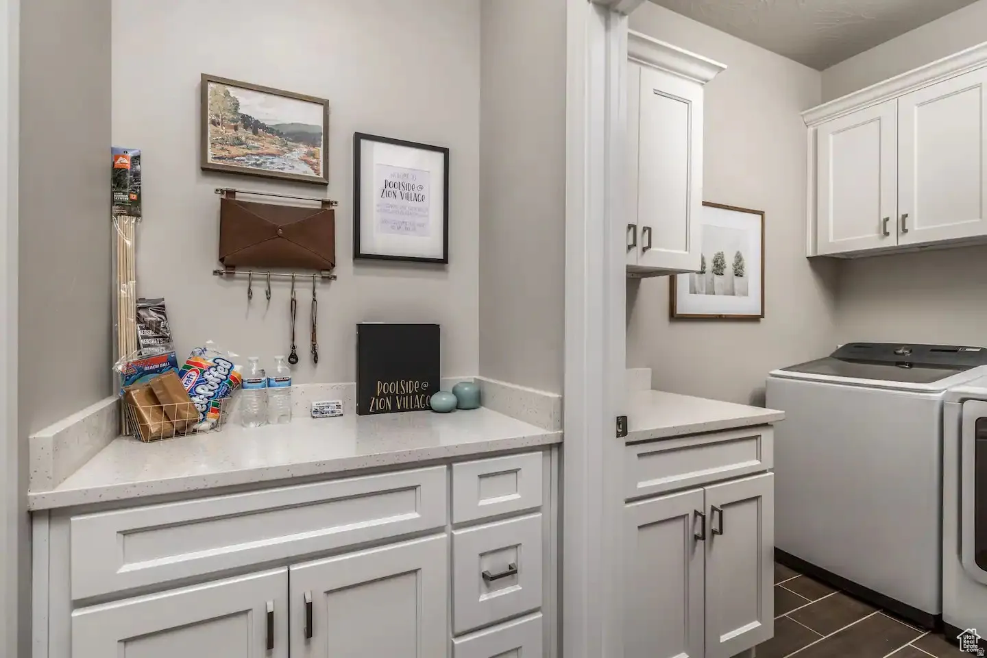 Laundry area featuring white shaker-style cabinetry, light-toned countertops, and dark tile flooring