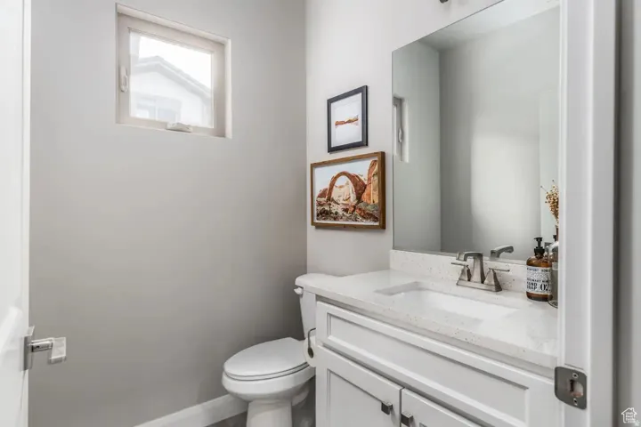 Powder room featuring a white single-sink vanity with a speckled countertop, a large wall-mounted mirror, a modern toilet, and a high-set window