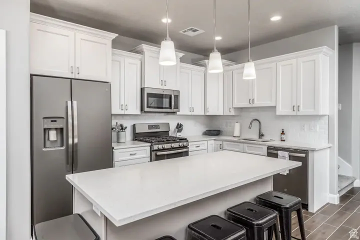 Modern kitchen featuring a central island with countertop seating, white shaker cabinetry, stainless steel appliances, and a subway tile backsplash