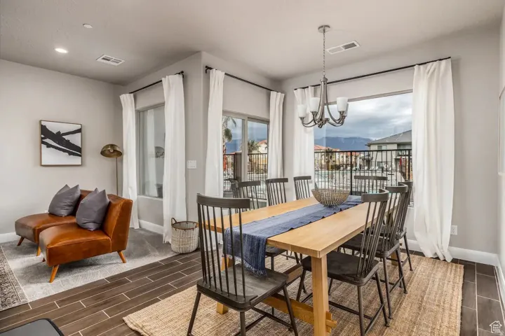 Spacious dining area featuring wood-finish flooring, a contemporary chandelier, large windows with a mountain backdrop, and light-toned wall paint