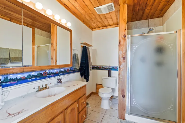 Bathroom featuring a wood-paneled ceiling, a double vanity with an integrated countertop sink, a full-width mirrored medicine cabinet with wood framing, a glass-enclosed shower, and tile flooring