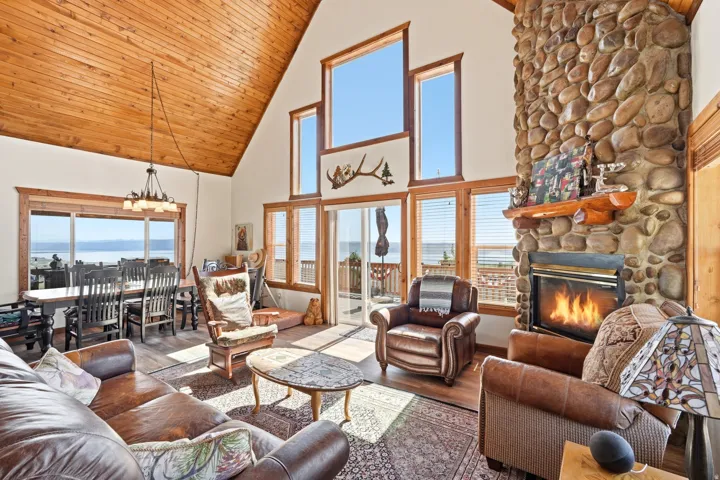 Spacious living area featuring a vaulted wood-paneled ceiling, a stone-faced fireplace with a wood mantel, and multiple windows