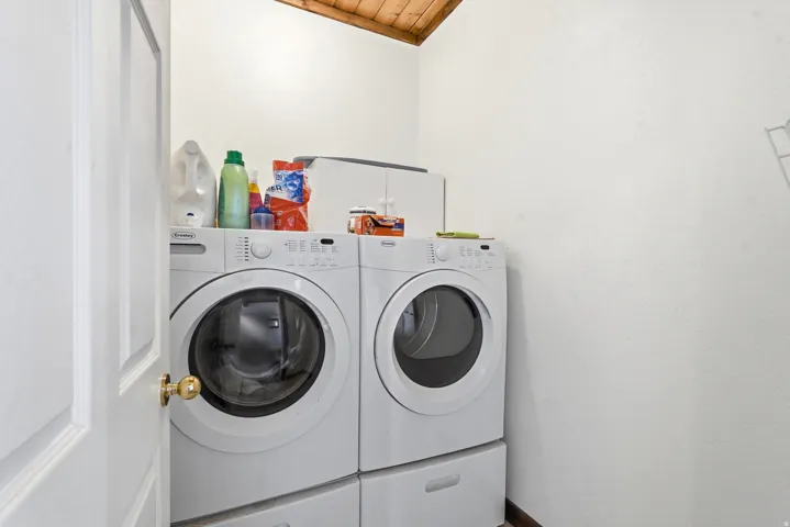 Laundry area with white walls, a wood-finish vaulted ceiling, and a white paneled door with a brass-finish knob