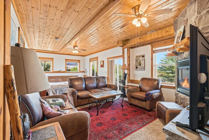 Spacious open-concept room featuring a wood-paneled ceiling, exposed wood beams, and multiple windows