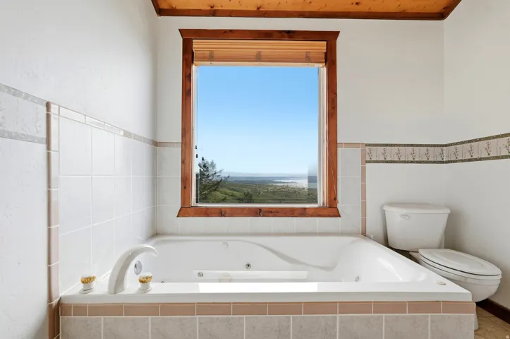 Jetted soaking tub with tile surround, wood-trimmed window, and wood-finish ceiling accent