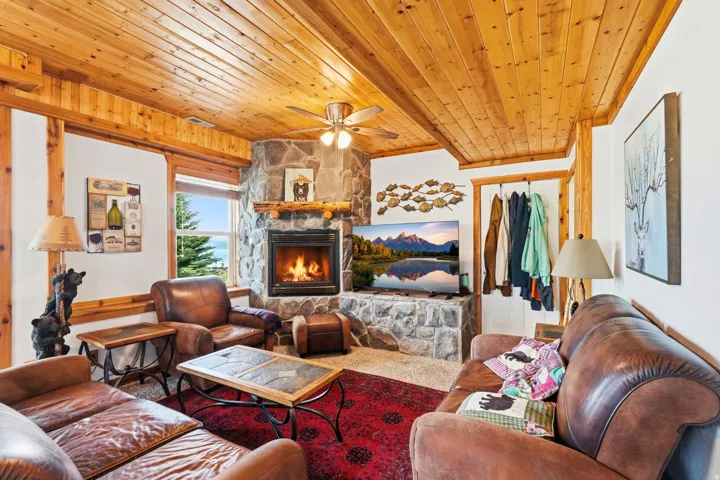 Living area featuring wood-paneled ceilings, a stone-clad fireplace, and a built-in stone media console