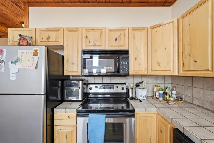 Kitchen featuring wood-finish cabinetry, tile countertops, and stainless steel appliances including an oven range and refrigerator