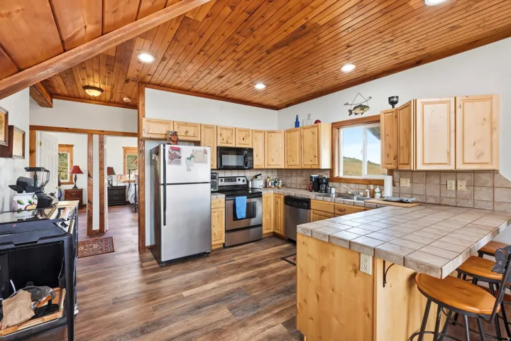 Kitchen featuring wood-finish flooring, natural wood cabinetry, stainless steel appliances, and a tiled countertop with an integrated breakfast bar