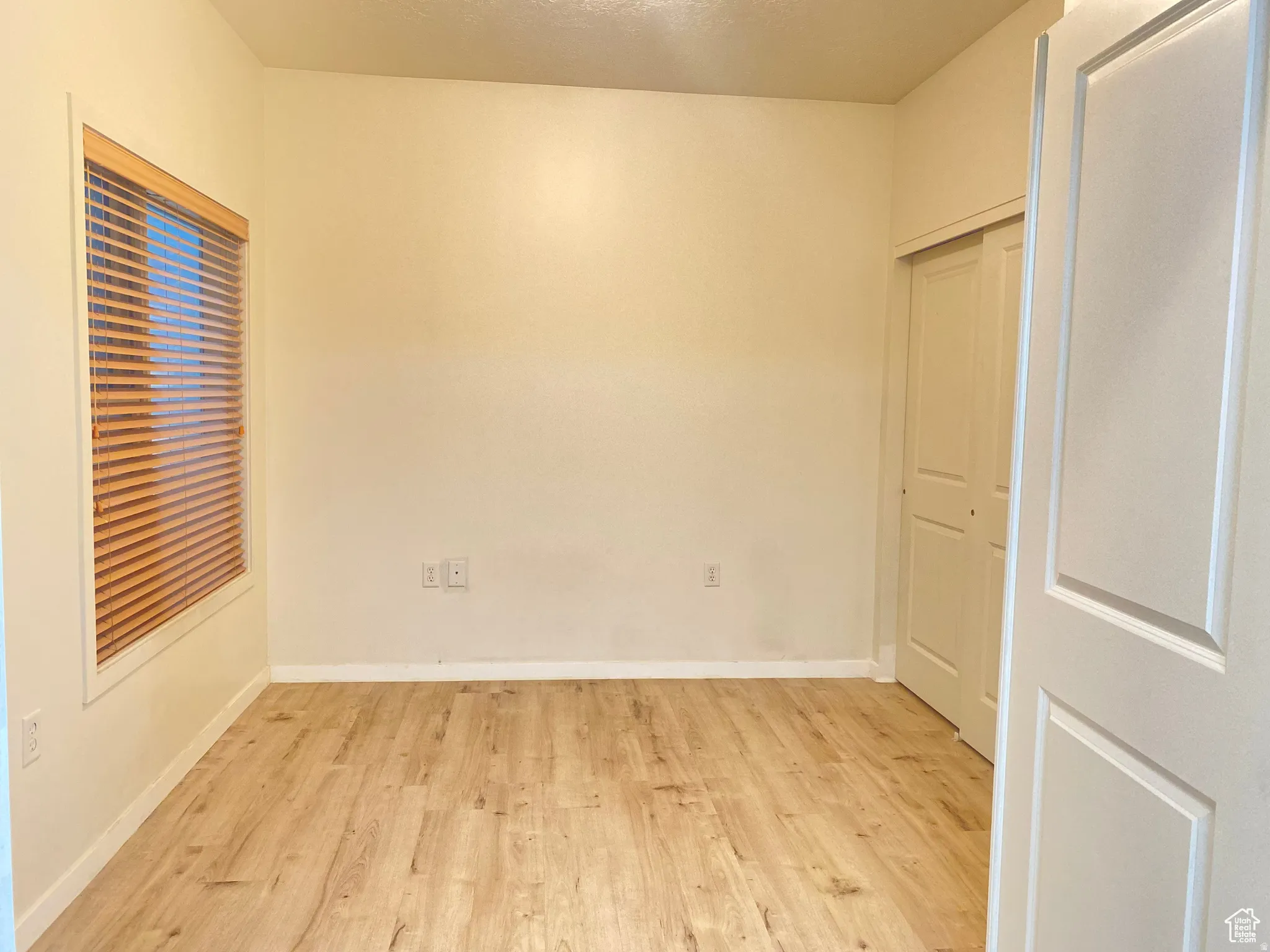 Light-filled room featuring wood-finish flooring, a window with wood blinds, and a built-in closet with bi-fold doors