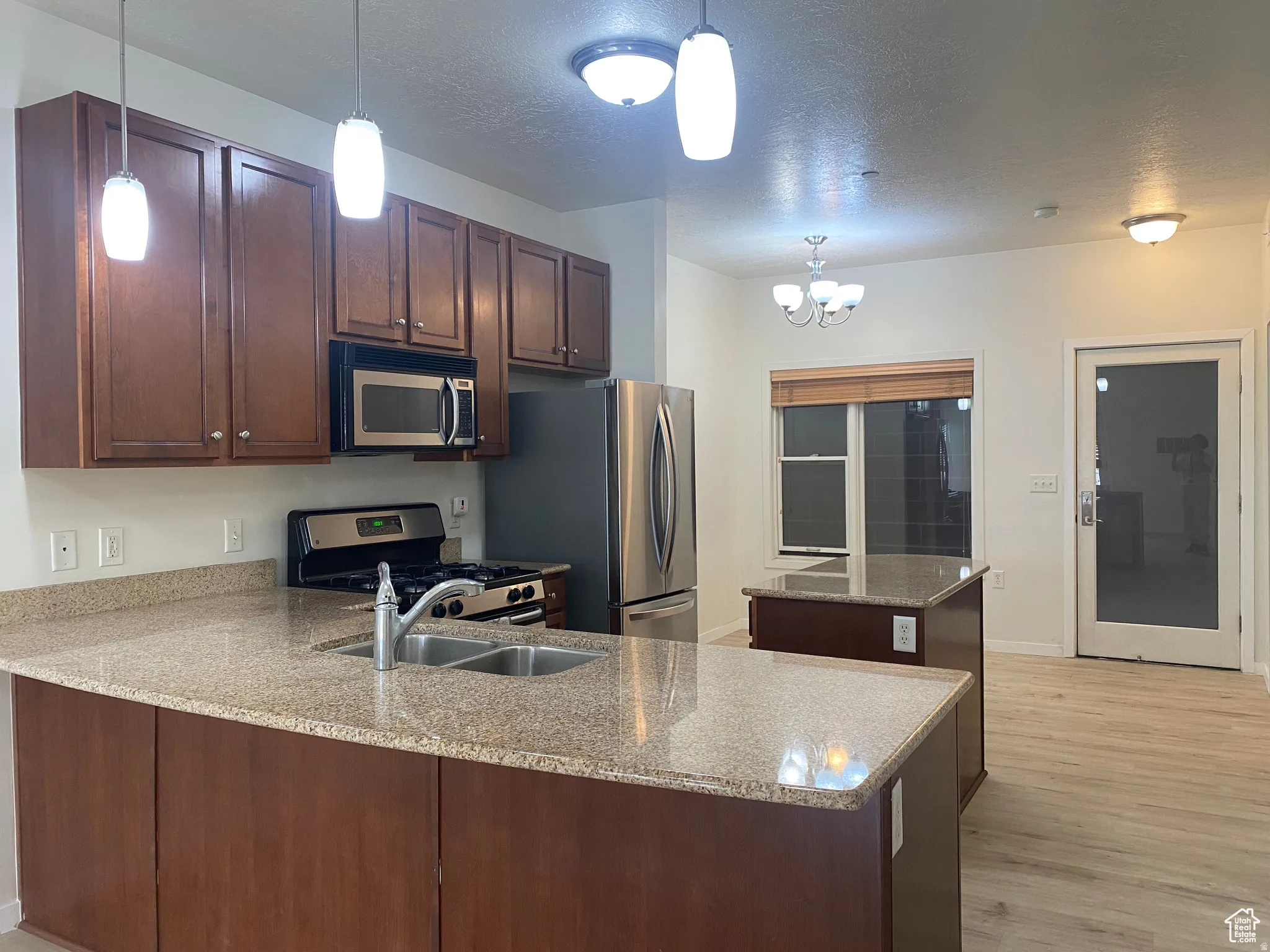Kitchen featuring wood cabinetry, light-toned granite countertops, and stainless steel appliances including a gas range, microwave, and refrigerator