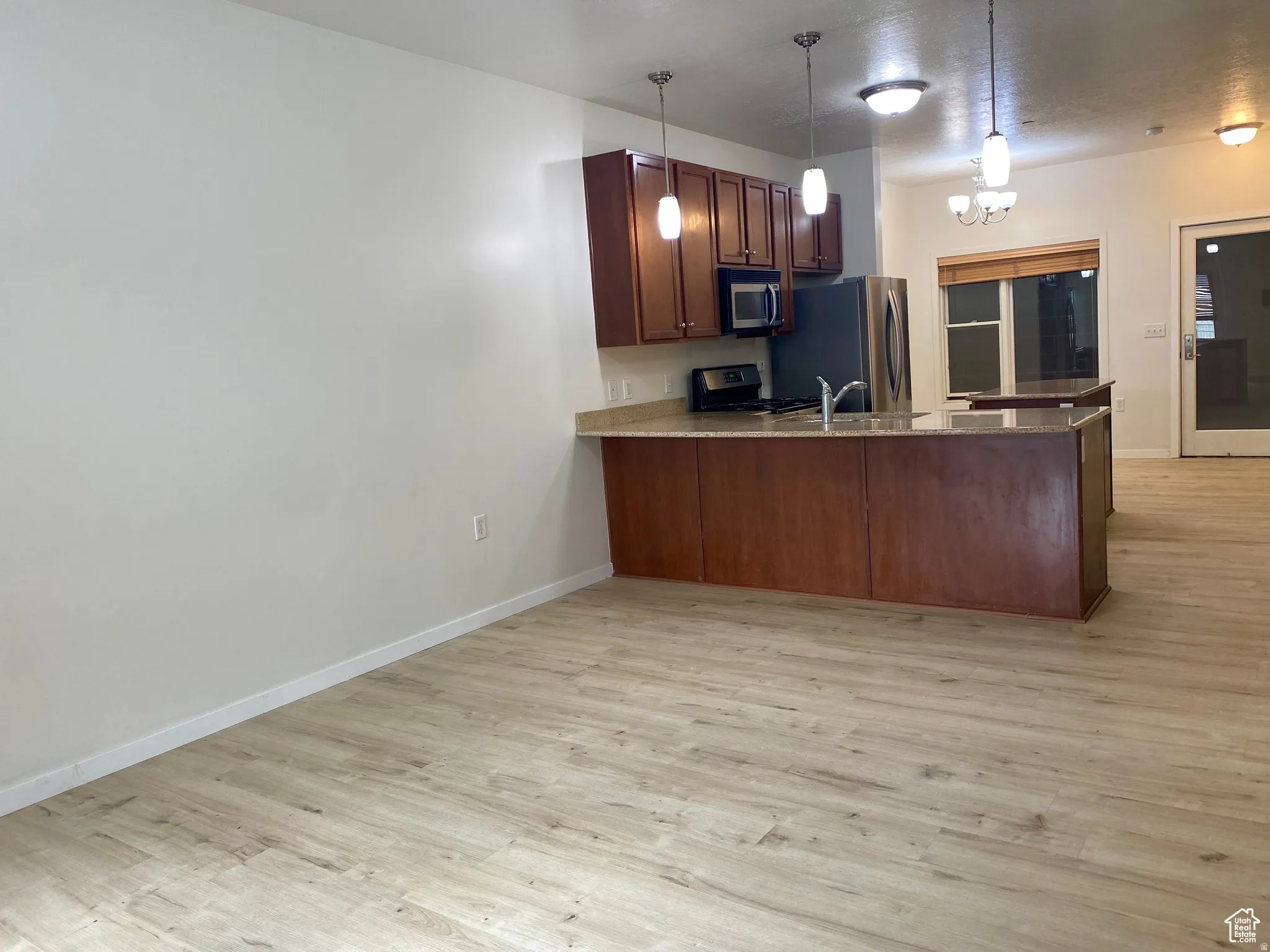 Open-concept kitchen featuring wood-finish flooring, dark wood cabinetry, light-toned countertops, stainless steel appliances, and pendant lighting over the island