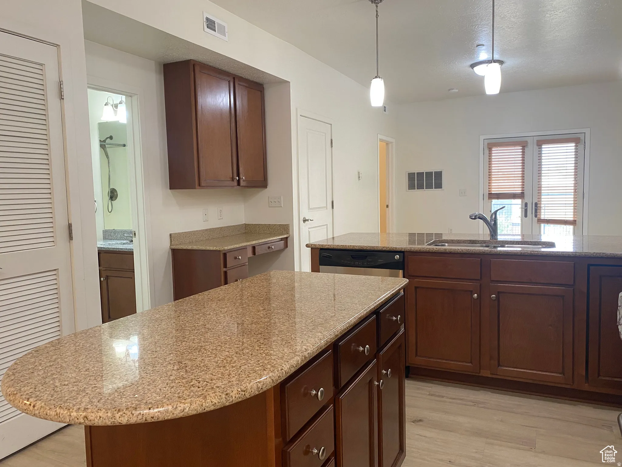Open-concept kitchen featuring two large islands with granite-style countertops, rich wood-finish cabinetry, a built-in stainless steel dishwasher, a double basin sink, and pendant lighting