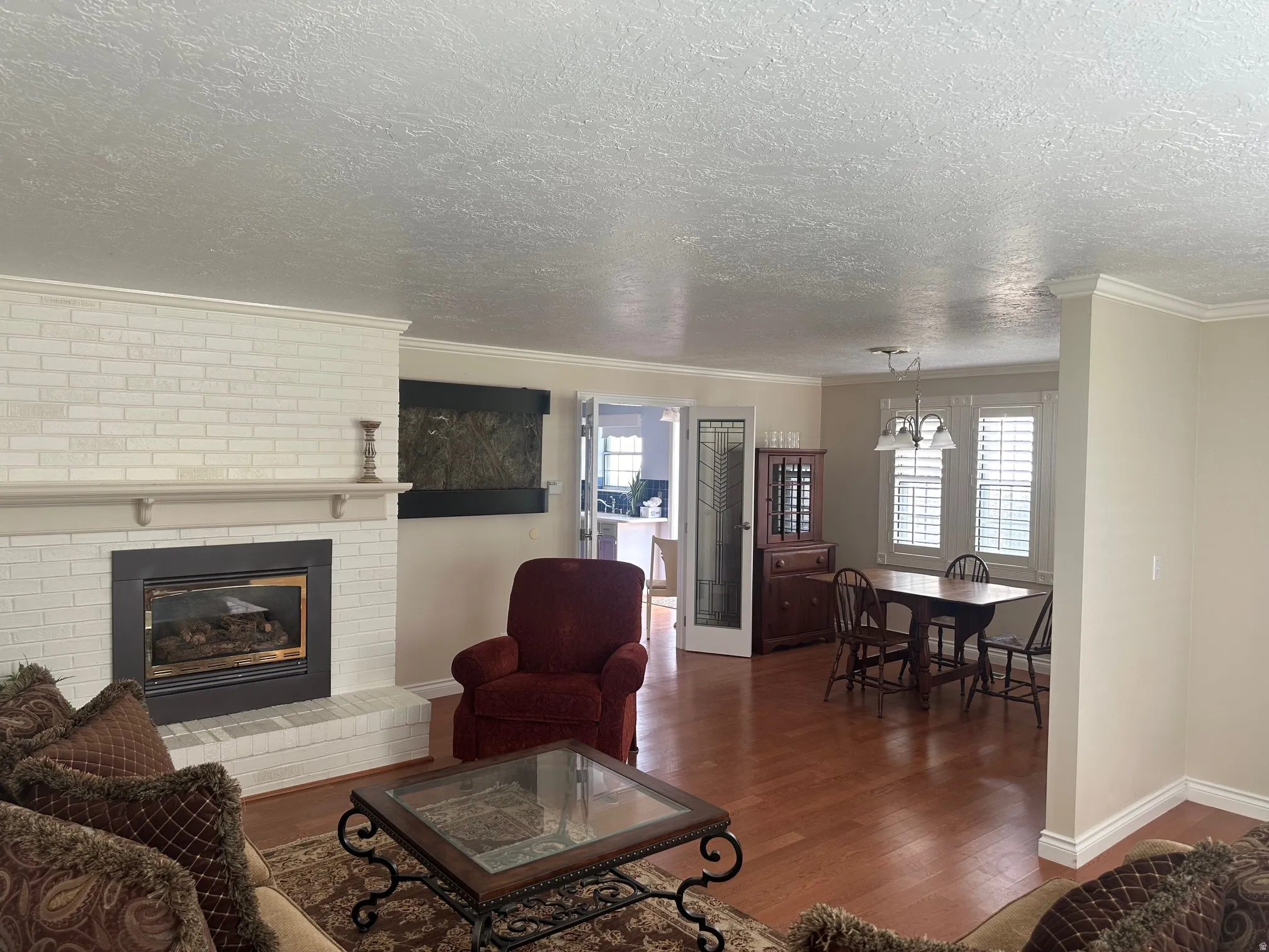 Brick-surround fireplace with a mantel, wood-finish flooring, and crown molding throughout