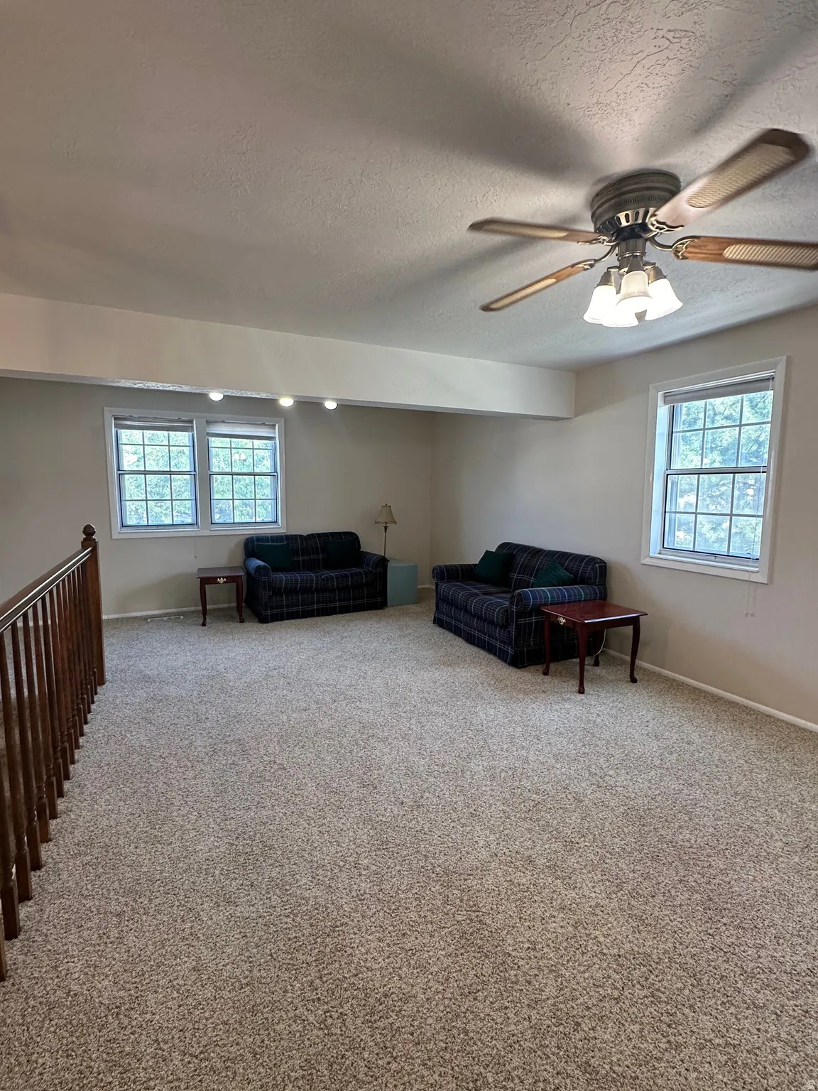 Spacious carpeted room featuring a ceiling fan with integrated lighting, track lighting, and multiple windows
