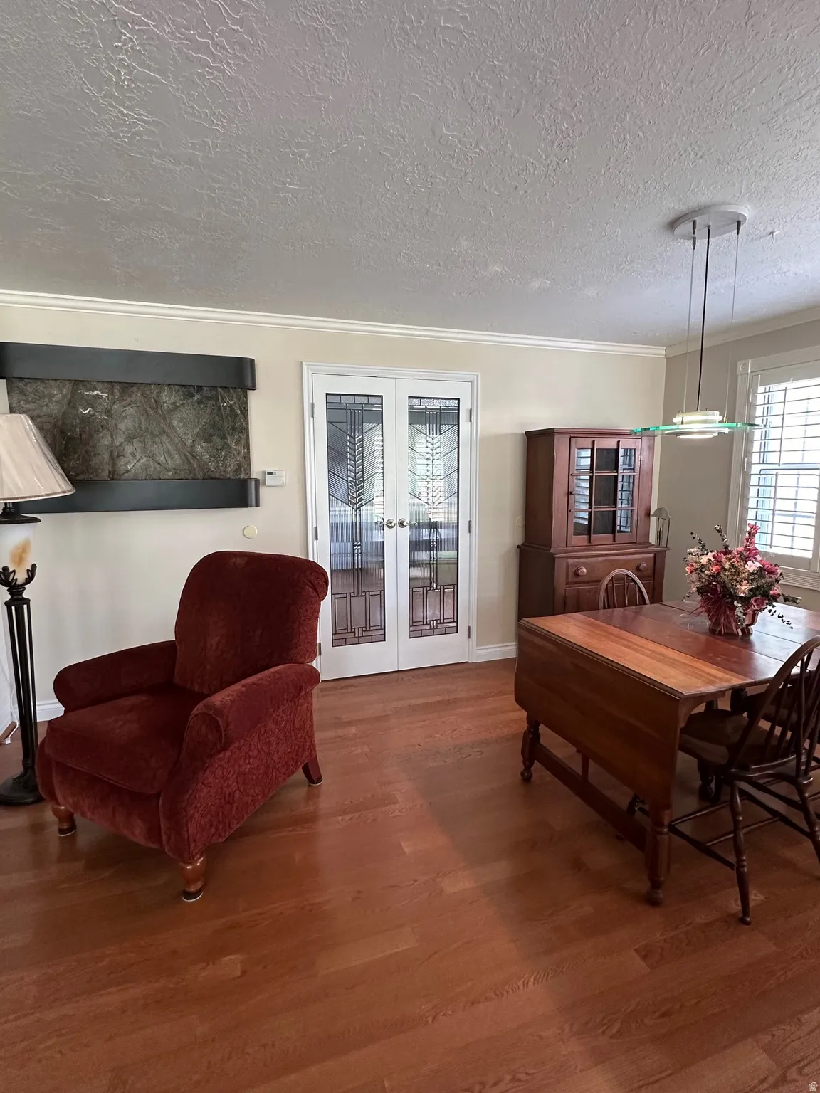 French doors with decorative glass panels, wood-finish flooring, crown molding, wall-mounted water feature, and plantation shutters