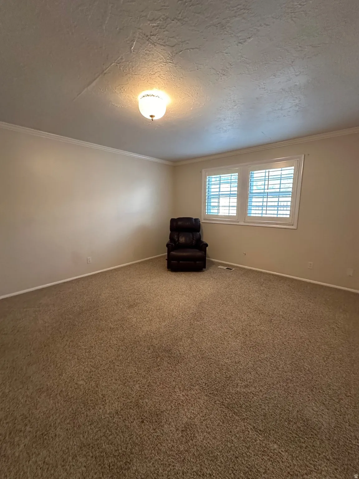Spacious room featuring neutral carpeting, light-colored walls, white baseboards, and white crown molding