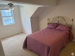 Carpeted room featuring a white-framed window, a ceiling fan with integrated lighting, and sloped ceiling details