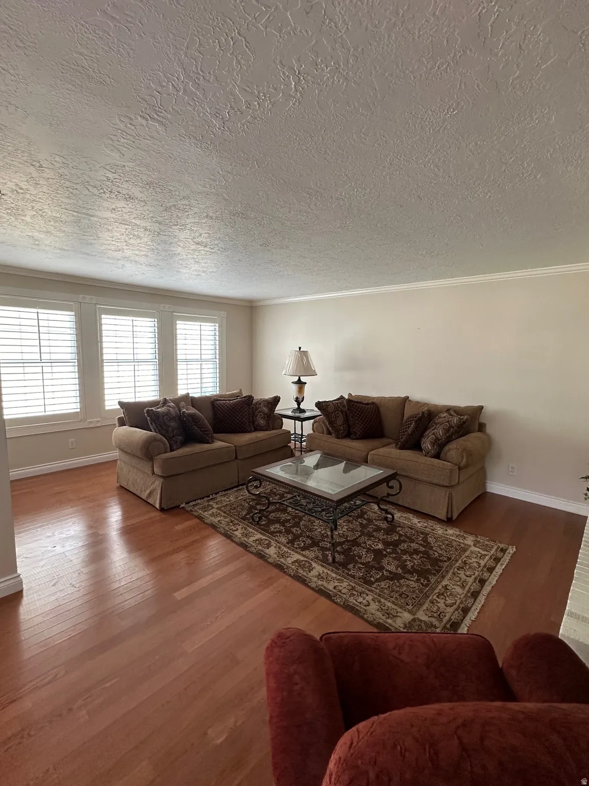 Hardwood flooring throughout the room, showcasing multiple windows with plantation shutters, crown molding, and textured ceilings