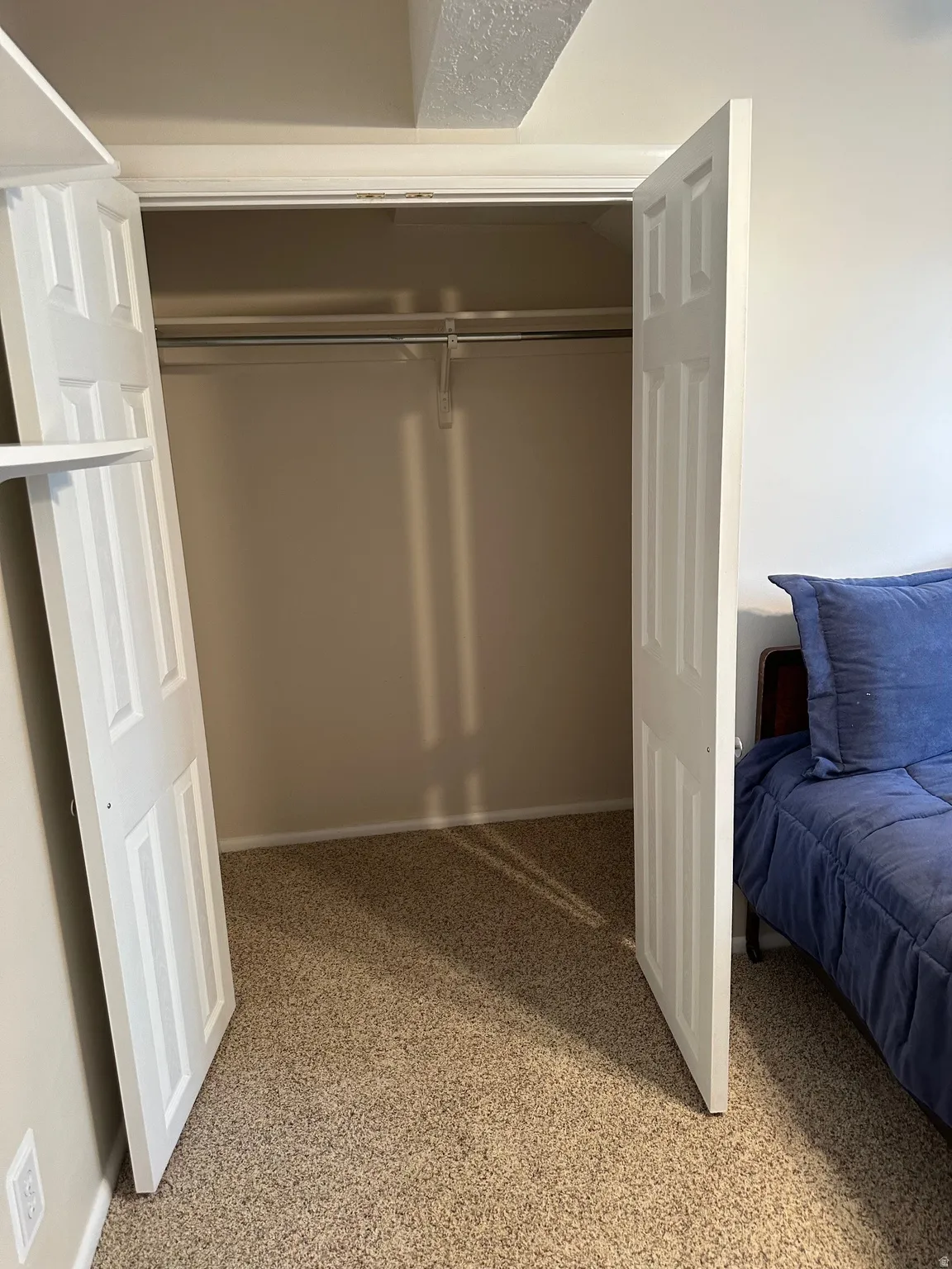Interior closet with bi-fold doors, white trim, a single hanging rod, and light-colored carpet flooring