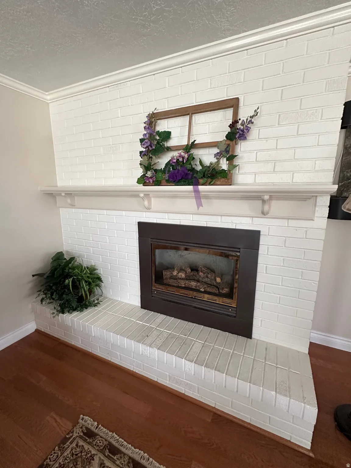 White-painted brick fireplace with a dark-framed insert, a substantial mantel shelf, and a raised hearth