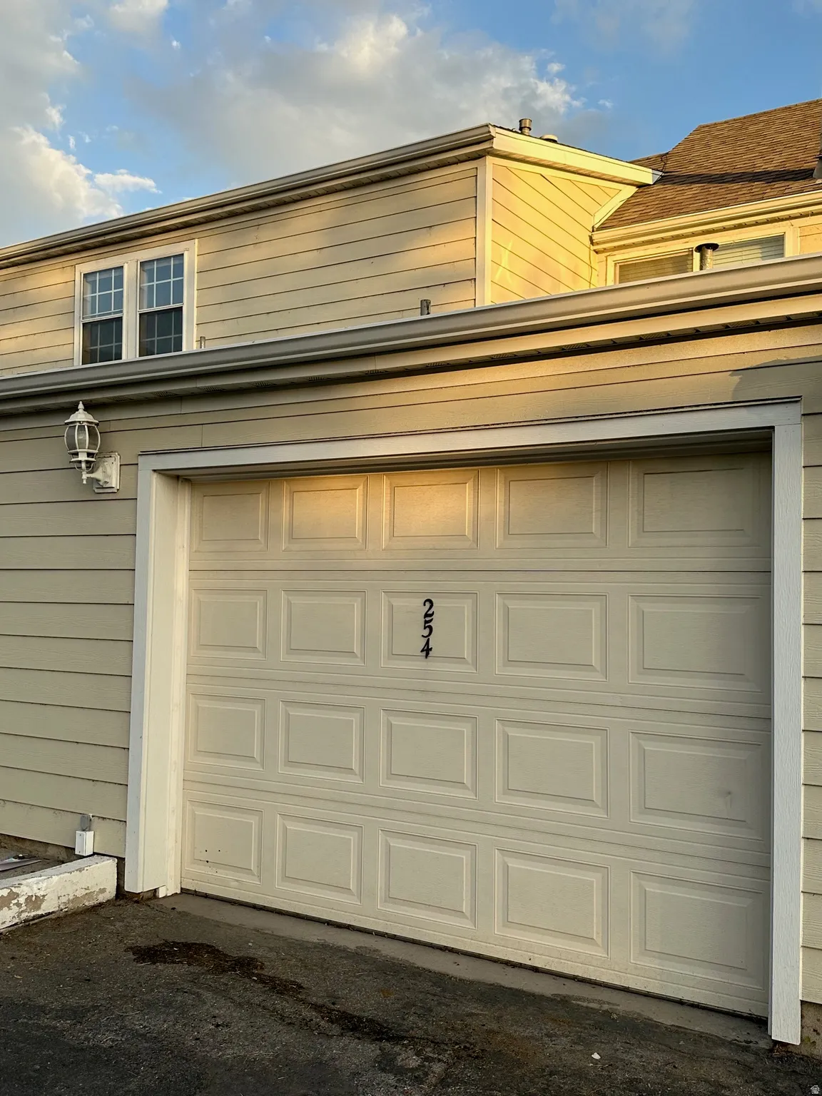 Attached garage with panel door, exterior wall lantern, house numbers, and light-colored siding