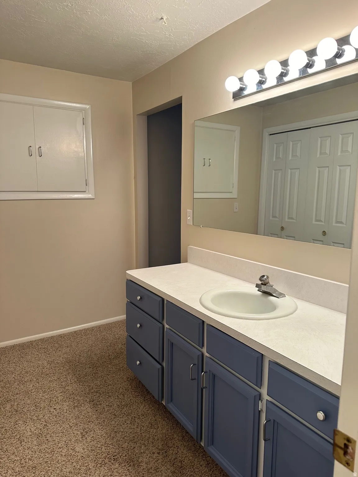 Bathroom vanity featuring a single basin sink, light-colored countertop, and a row of vanity lights
