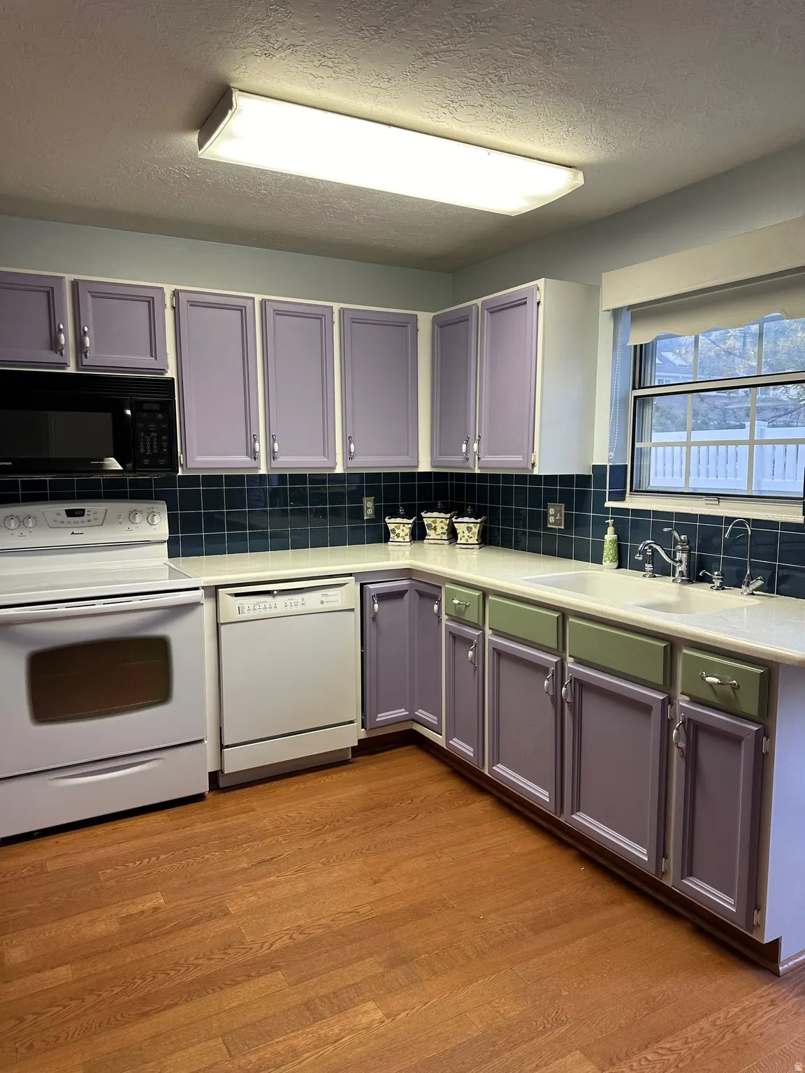 Kitchen featuring wood-finish flooring, a double basin sink, and a black built-in microwave