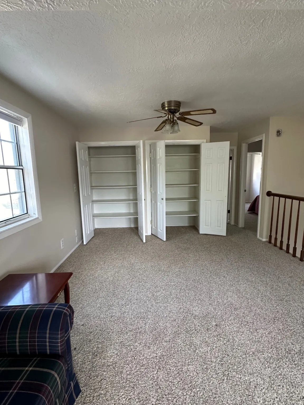 Carpeted interior space featuring two built-in storage closets with bi-fold doors, a ceiling fan, and a window providing natural illumination
