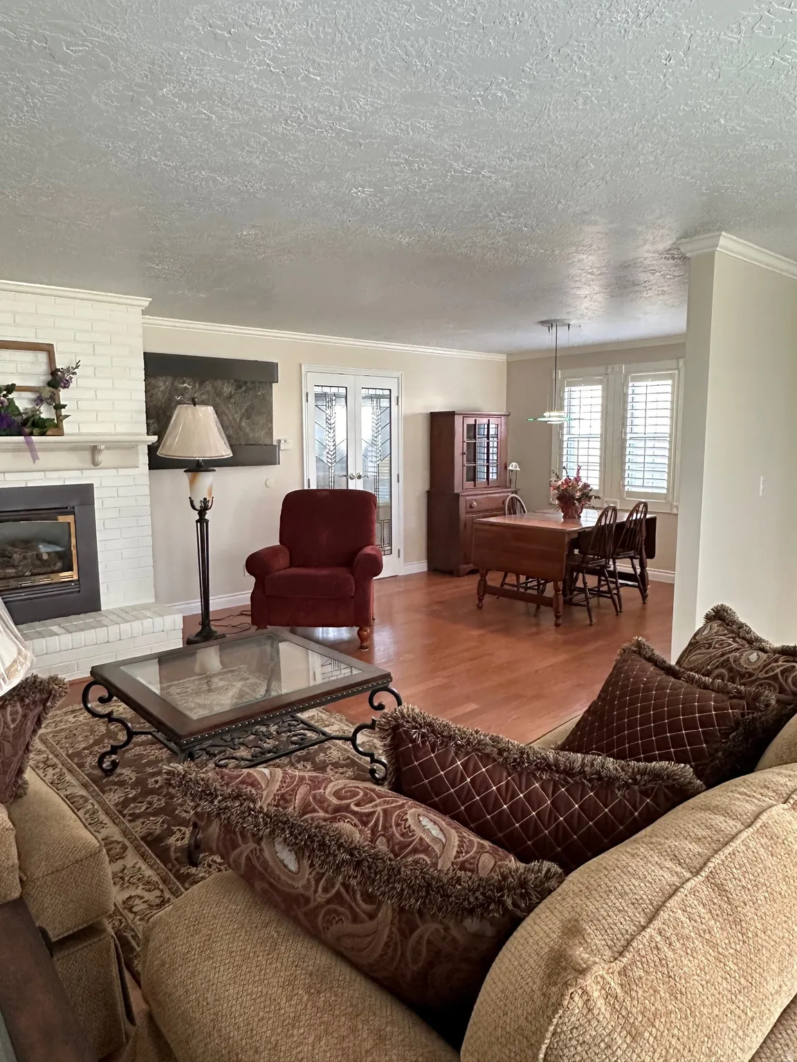 Open-concept living area featuring wood-finish flooring, a white brick fireplace, and crown molding