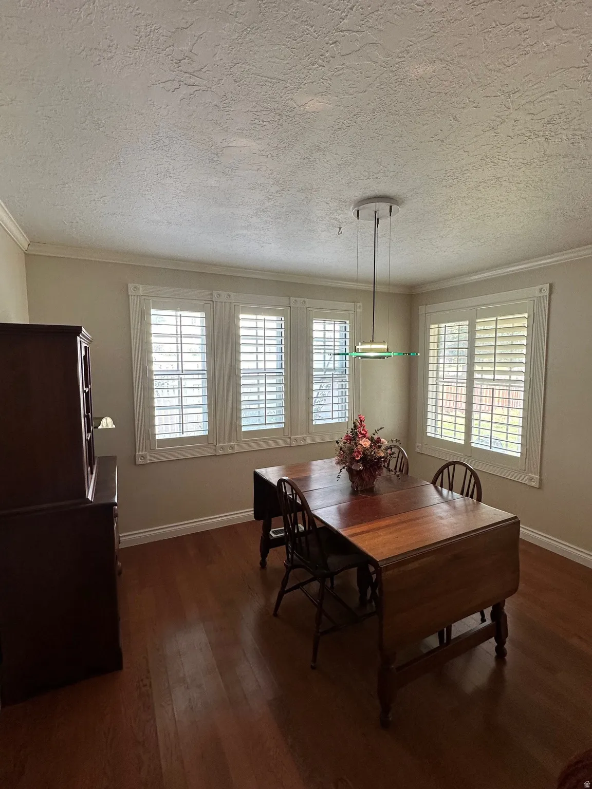 Room featuring wood-finish flooring, crown molding, and a contemporary pendant light fixture